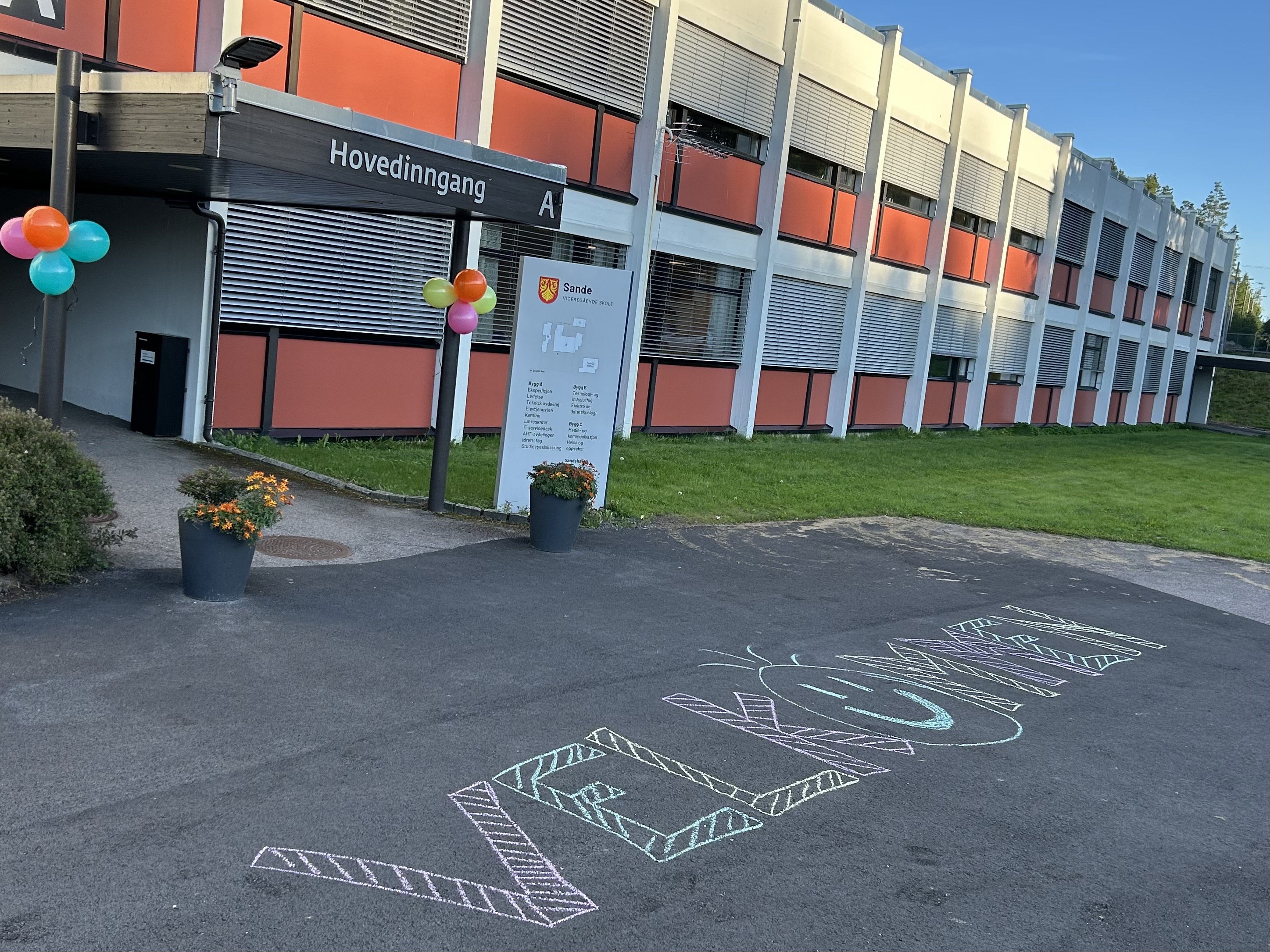 Skolebygning med "velkommen" skrevet med kritt på asfalt foran hovedinngangen
