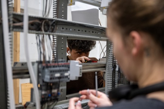 Ei jente og en gutt som jobber på hver sin side av et elektrisk anlegg.
