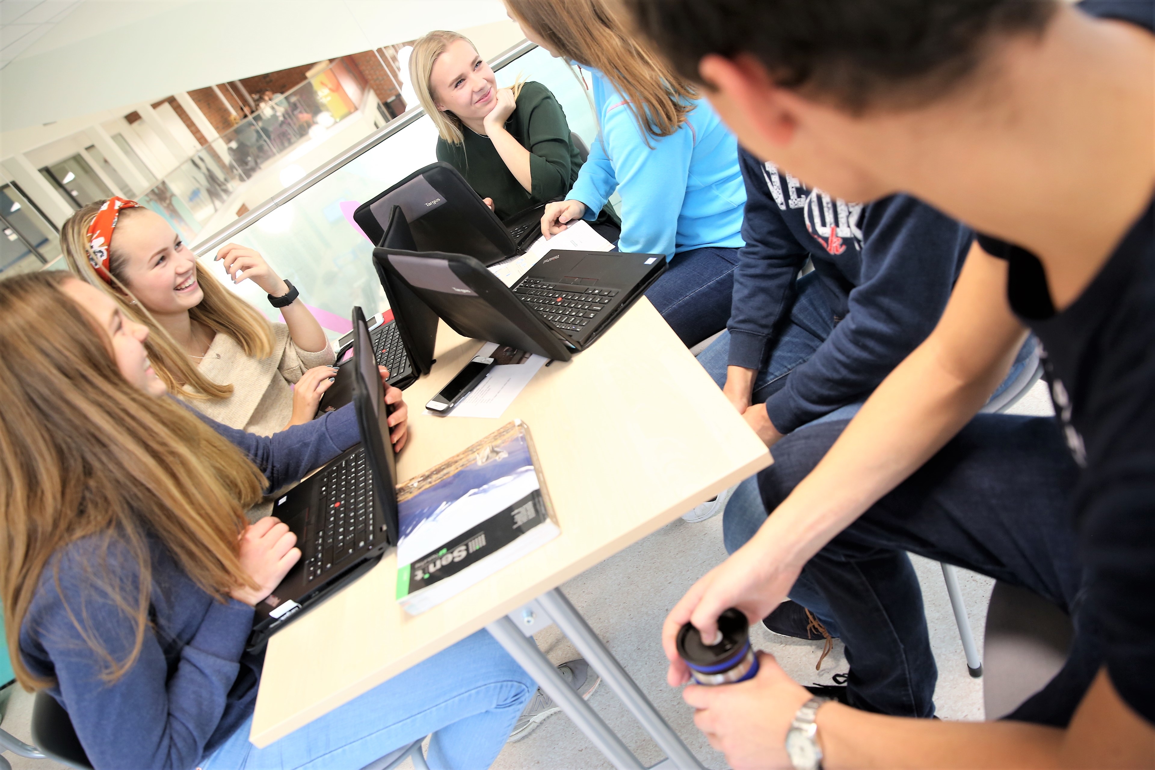 Bilde av smilende ungdommer som sitter rundt et bord ,ed PC og skolearbeid.