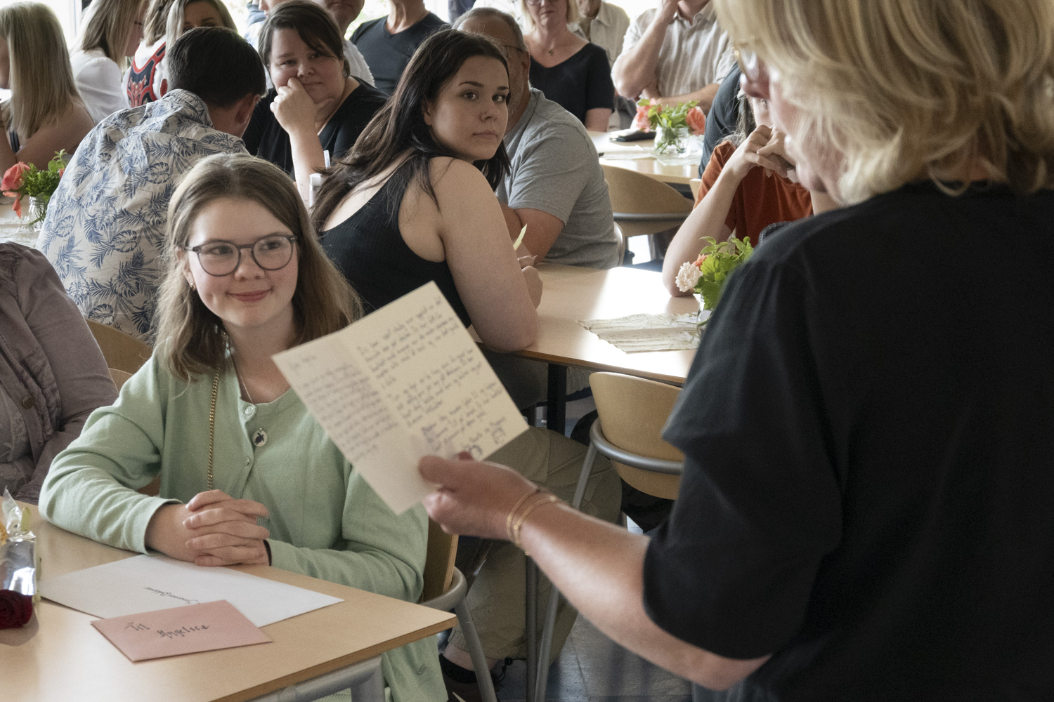 Elever og foresatte sitter rundt bord, inne.