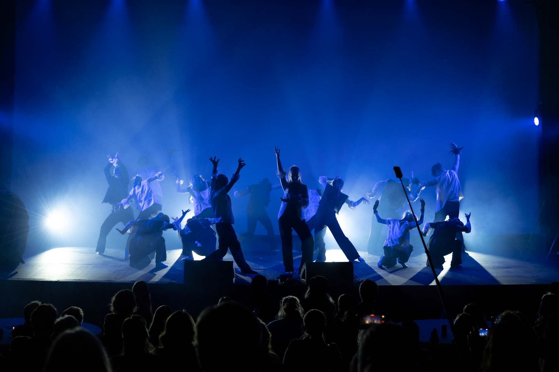 Mange dansere på en scene. Kraftige skygger i blått lys.