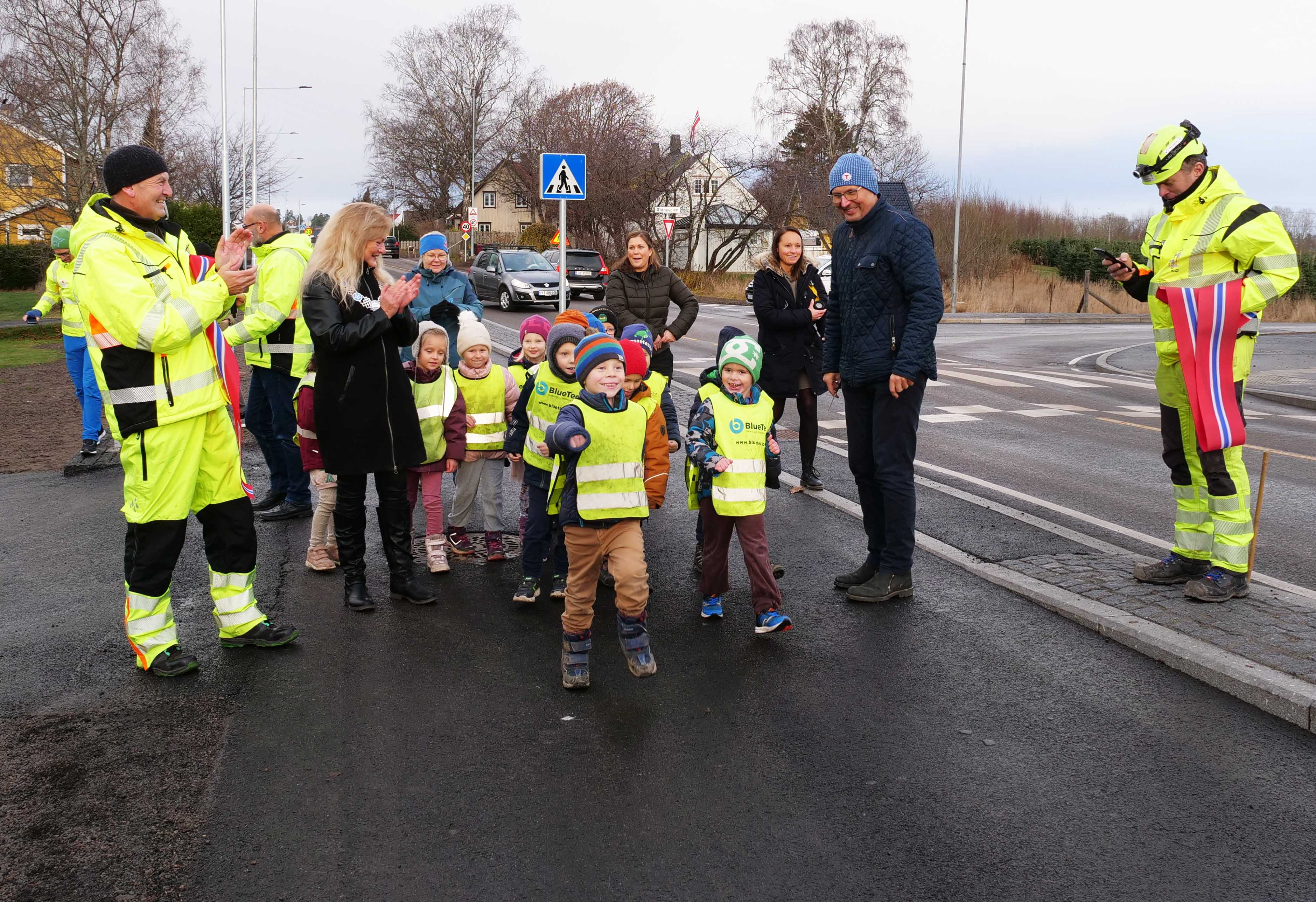 En gruppe førskolebarn går mot fotografen, mens voksne representanter for utbygger ser på og applauderer.