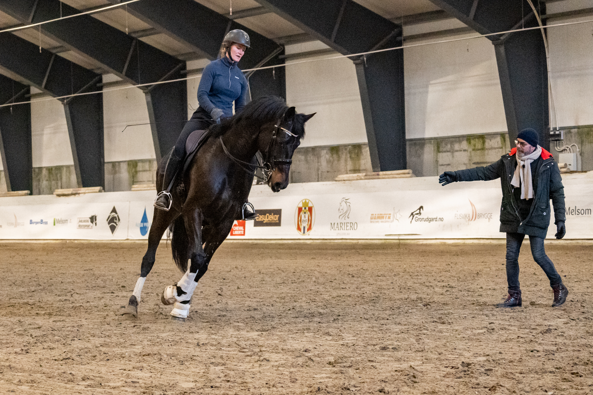 Dressurrytter instrueres av trener i ridehall