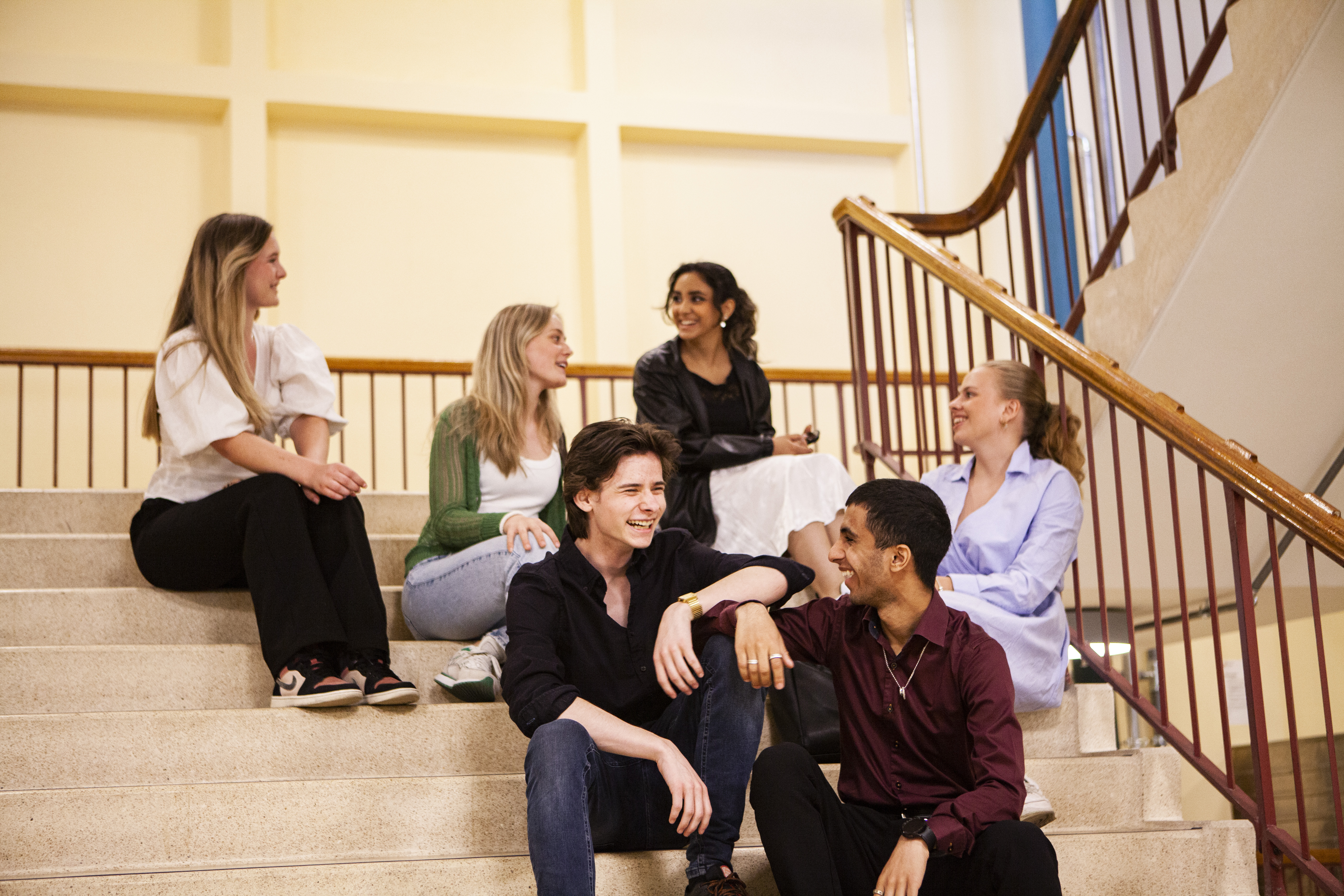 Gutter og jenter som sitter i en trapp. Alle smiler og har det bra sammen.
