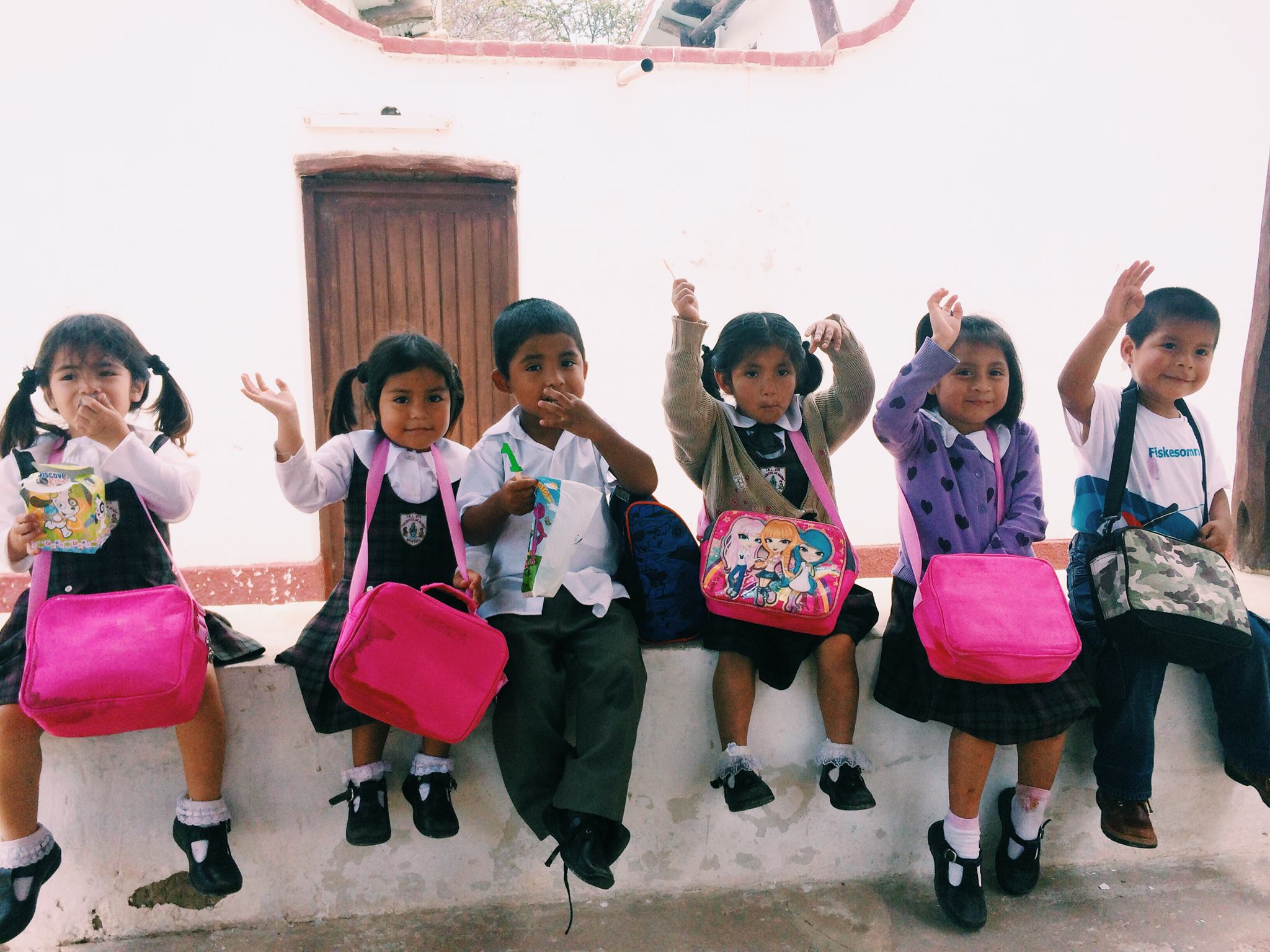 Illustrasjonsbilde: Små barn sitter på en murkant og vinker til fotografen.