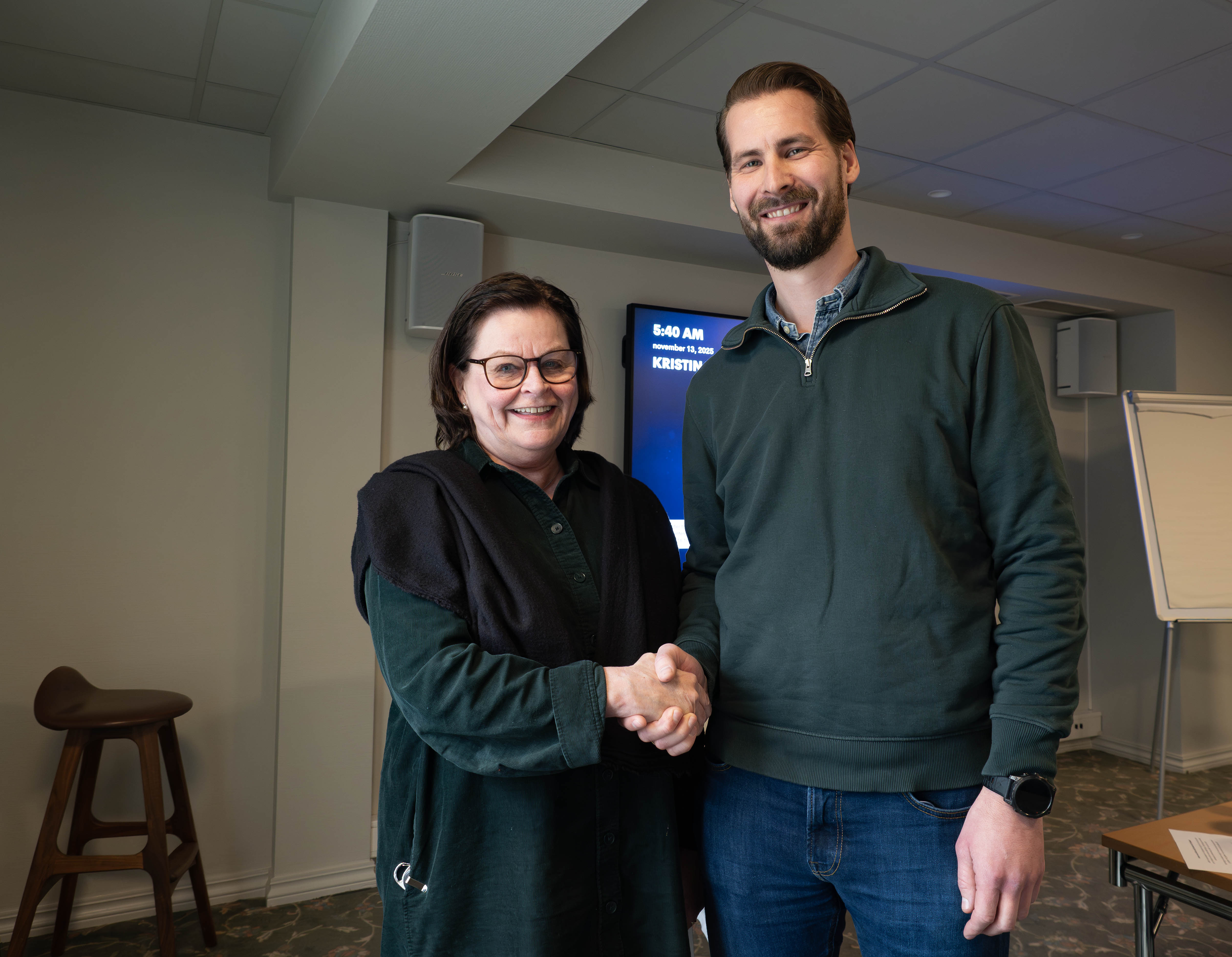 Fylkesdirektør Toril Eeg og direktør for prosjektgjennomføring i HENT AS, Erik Tveit, gratulerer hverandre med kontrakt i et møterom