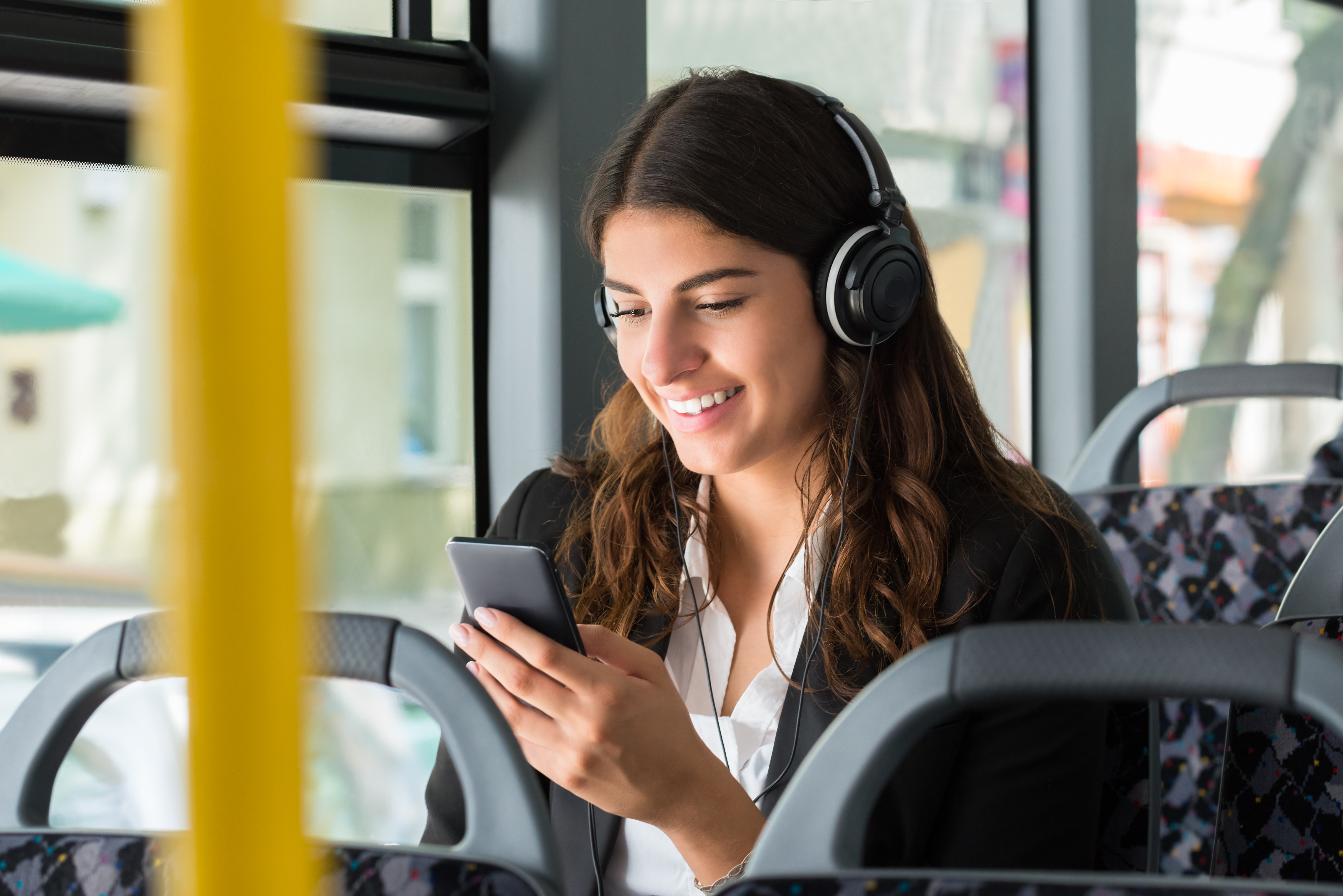 Smilende jente sitter på buss. Busseter synlig i forgrunn av bildet.