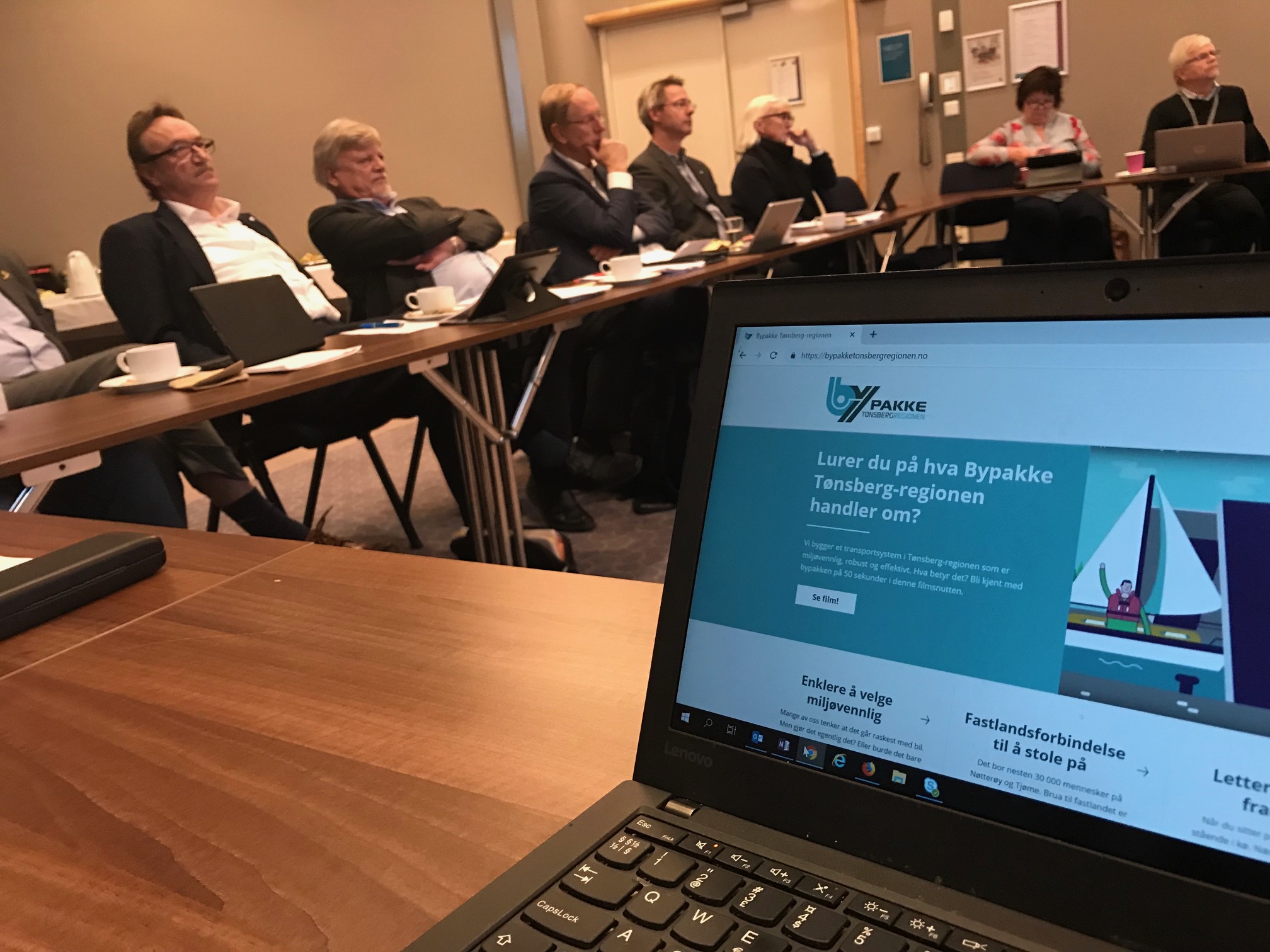 Foto av dataskjerm med bypakketonsbergregionen.no og politikere i Overordnet styringsgruppe i bakgrunnen