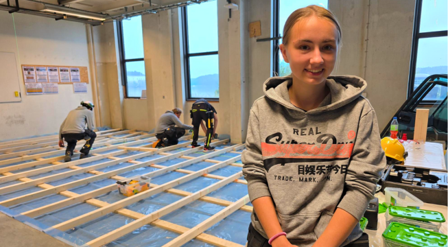 Jente står foran medelever som bygger gulv