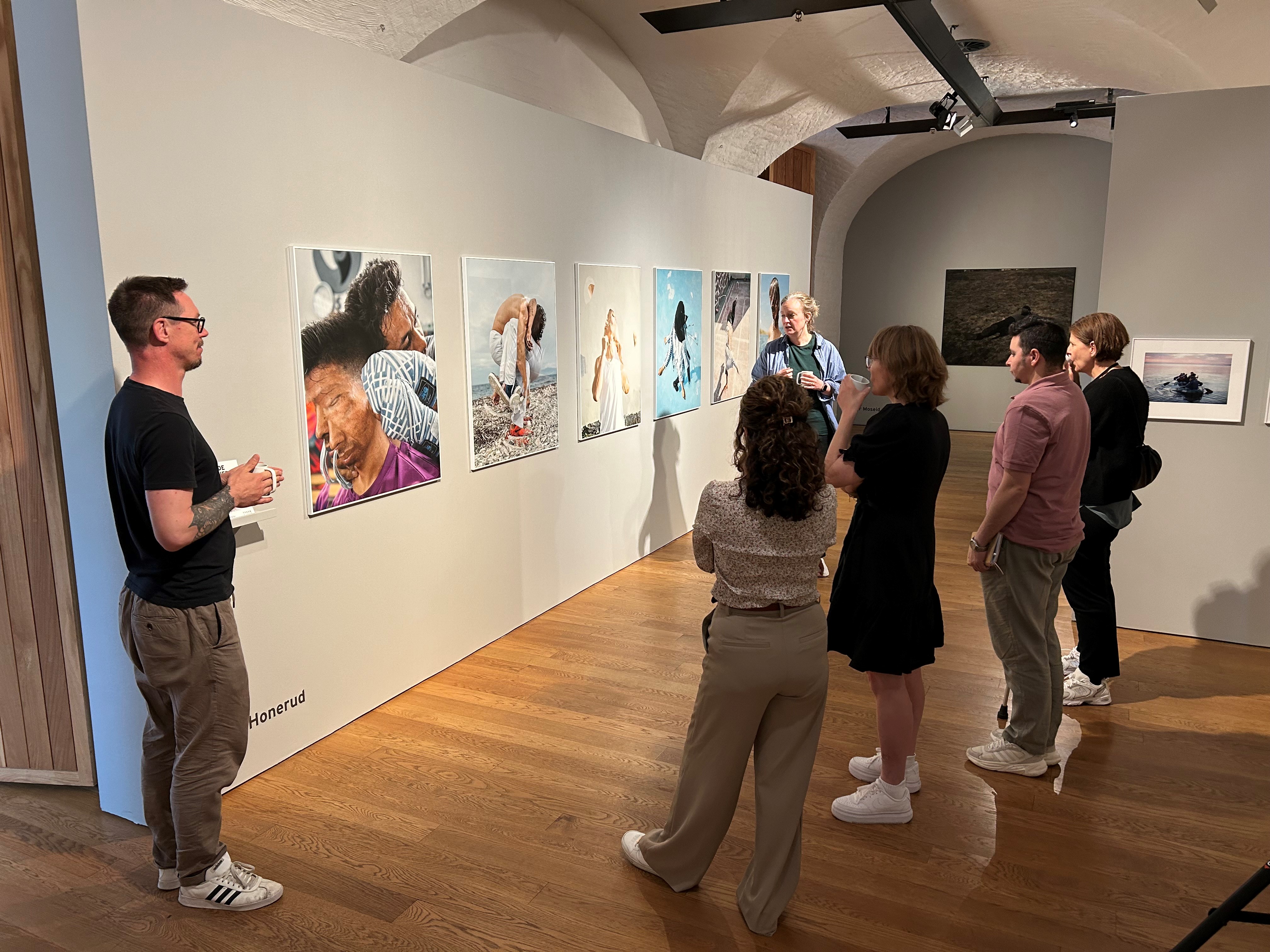 Mennesker på omvisning på Preus fotomuseum ser på vegg med uttrykksfulle fotografier