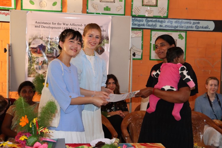 To jenter fra videregående gir et bevis til en mor med et barn på armen.