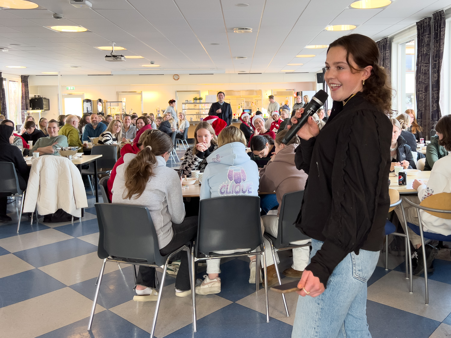 Mange mennesker sitter på stoler rundt mange bord i et stort rom