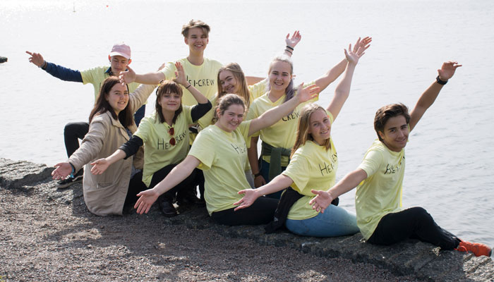 Ni ungdommer sitter ved sjøen ikledd gule t-skjorter