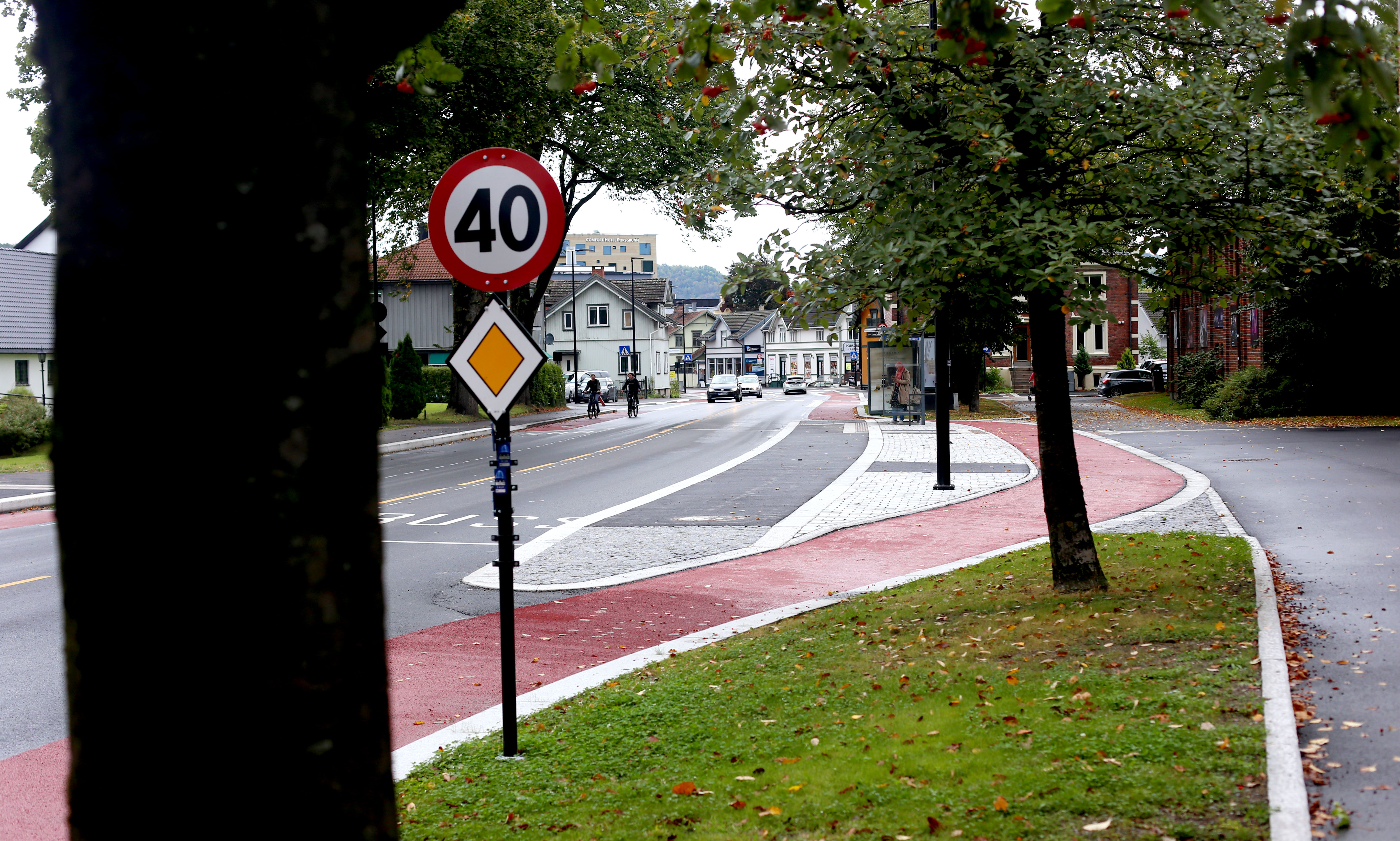 Hovedmotiv er vei som forsvinner innover i bildet, der rødt sykkelfelt slynger seg forbi bussholdeplass.