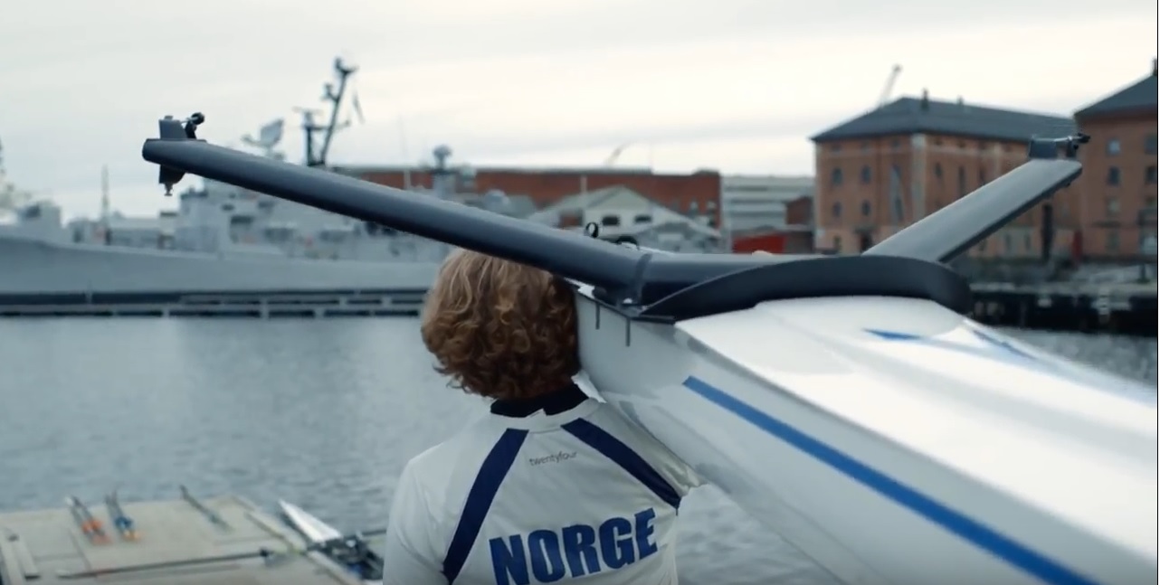 En roer bærer båten på skuldra på vei mot vannet