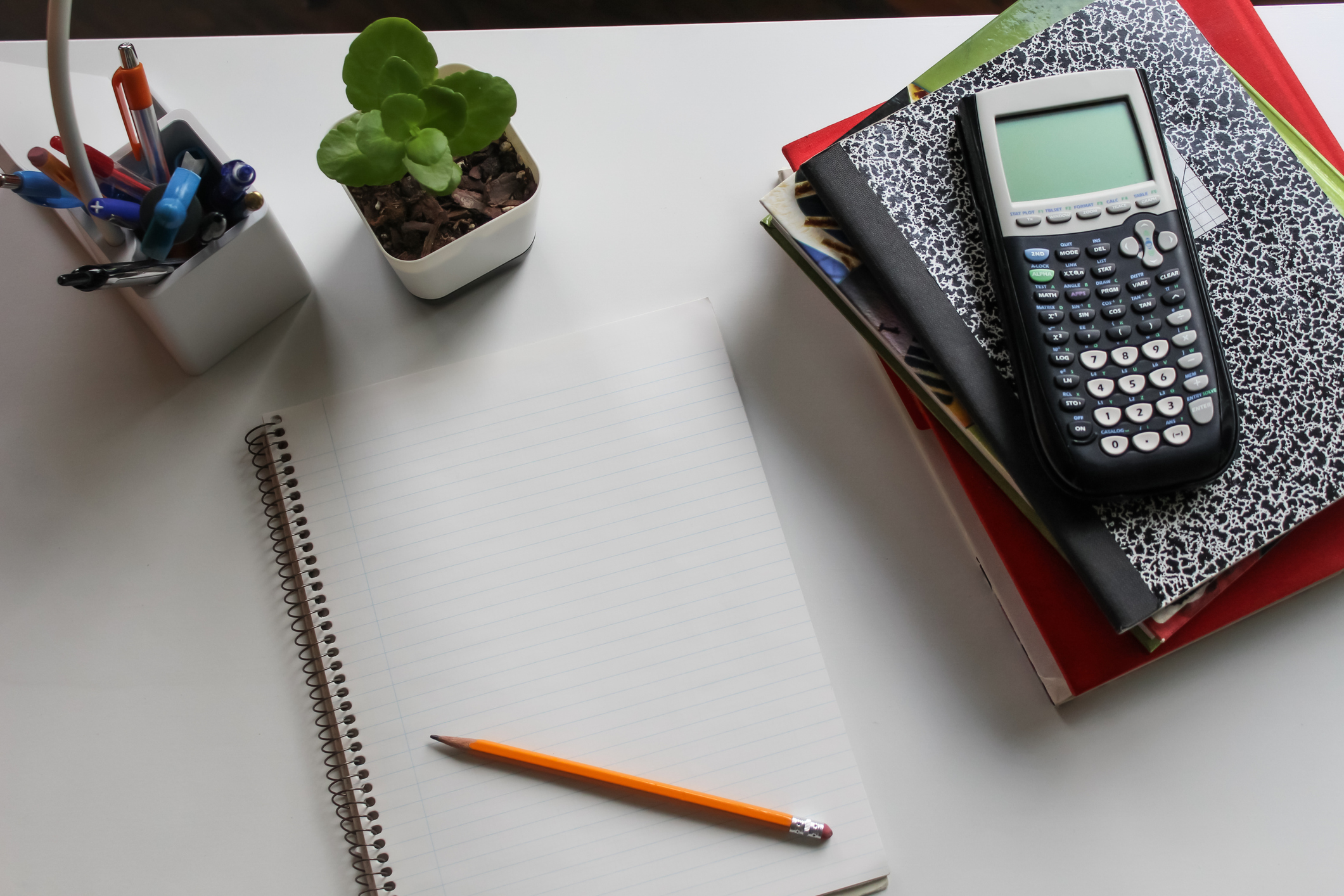 Bilde av skriveblokk med blyant og kalkulator og bøker på ett skrivebord.