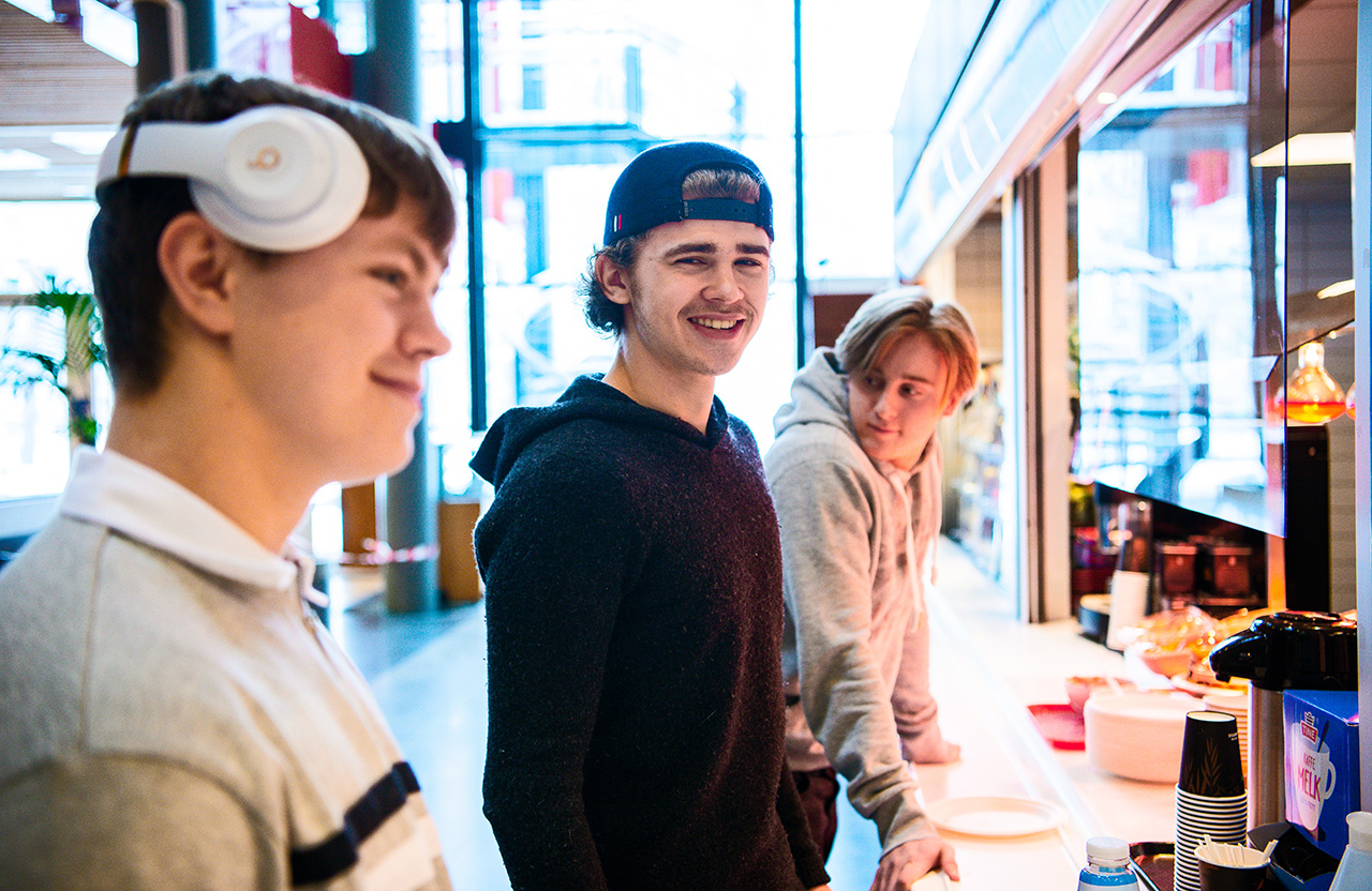 Tre ungdommer står i kantine i et skolebygg.