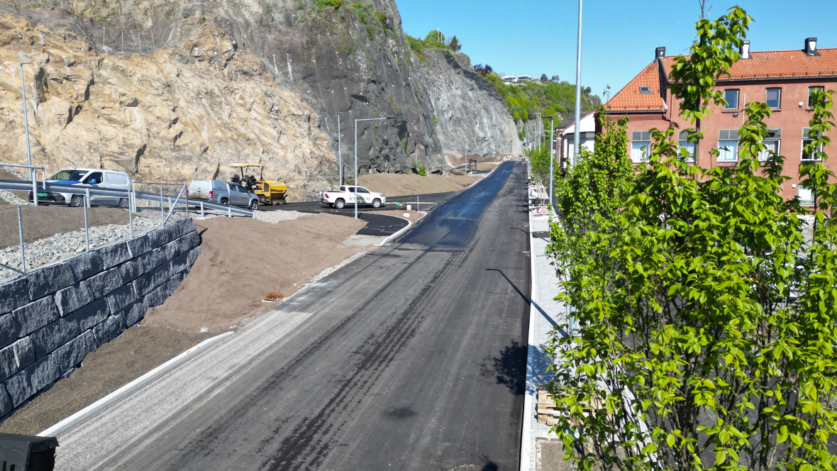 Den nye fylkesveien med ny asfalt, nybygde støttemurer og en del anleggsbiler. Tatt nordover med nyplanta trær i høyre bildekant.