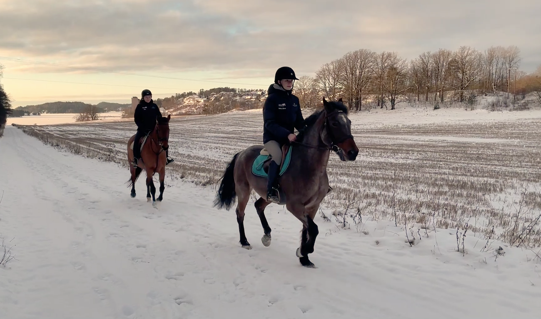 To elever rir på hver sin hest i vinterlandskap