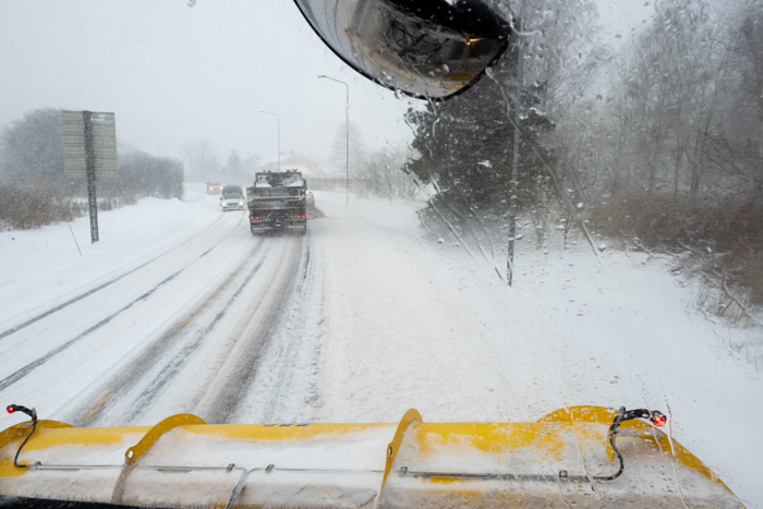 Bilde tatt innenfra en brøytebil som brøyter bak en annen brøytebil.