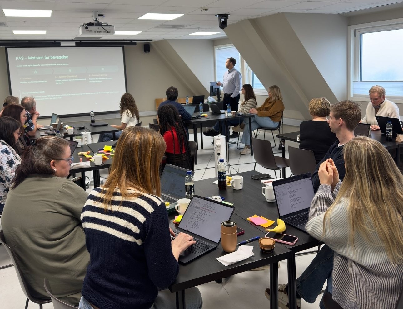 Deltakere rundt gruppebord følger med på kursholder og presentasjon