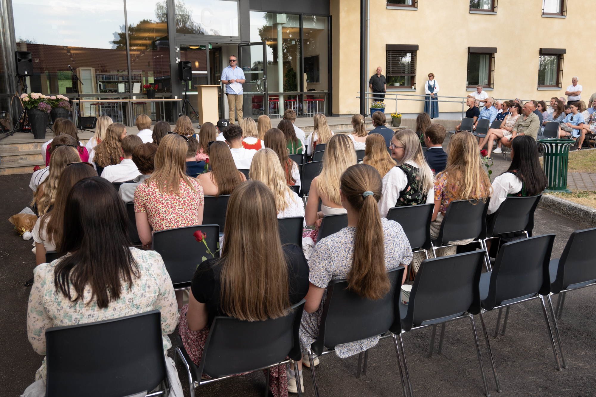Avgangselevene sitter på stoler ute på plassen og lytter til en tale