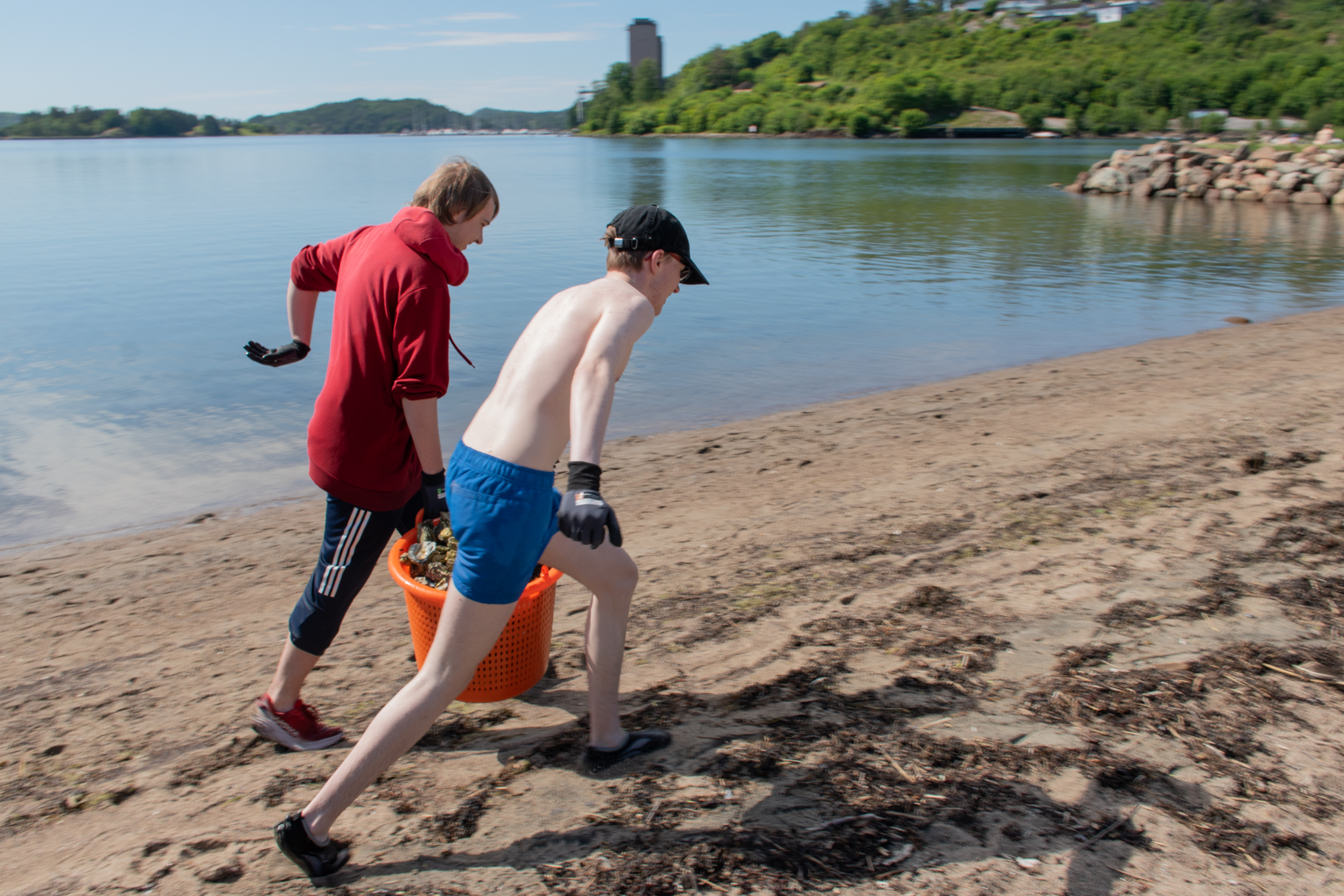 To gutter løper med en kurv full av østers mellom seg, langs stranda.