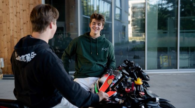 To unge menn på motorsykler foran bygg