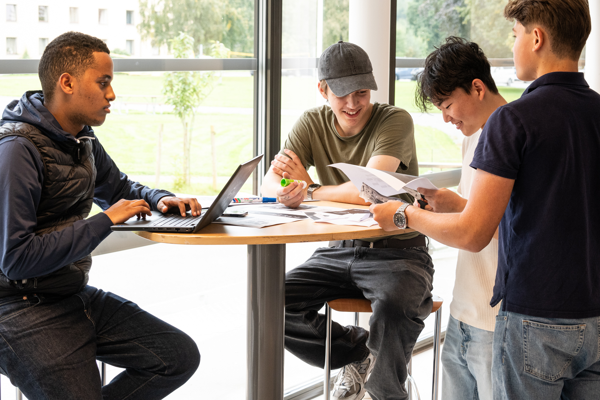 Fire elever jobber rundt et bord, inne.