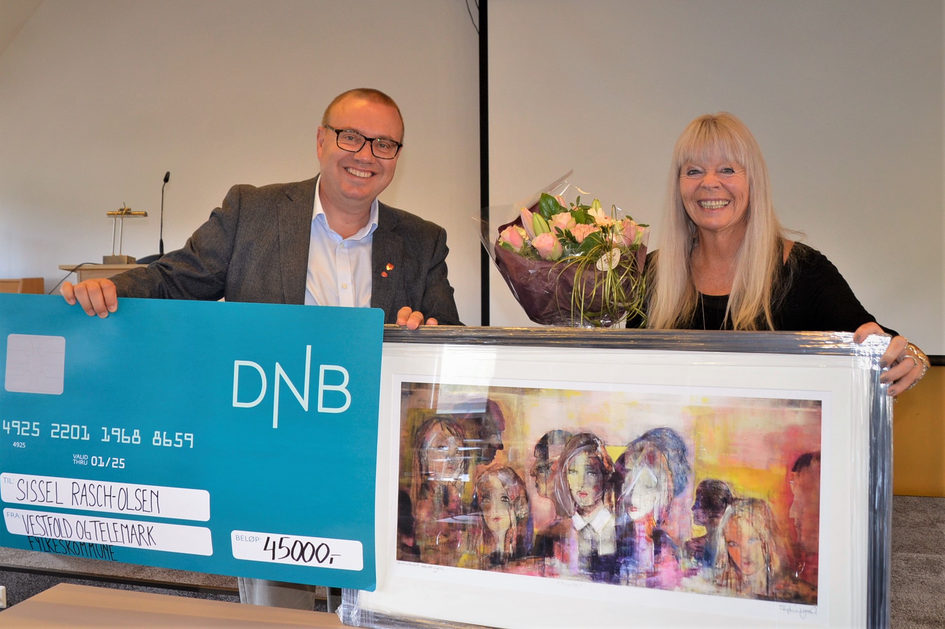 Hovedutvalgsleder og fjorårets prisvinner holder frem sjekken og kunstverket prisvinner fikk.