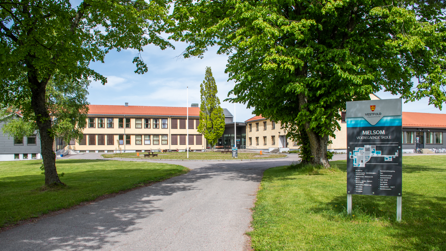 Skolebygningene med grønn plen og trær foran