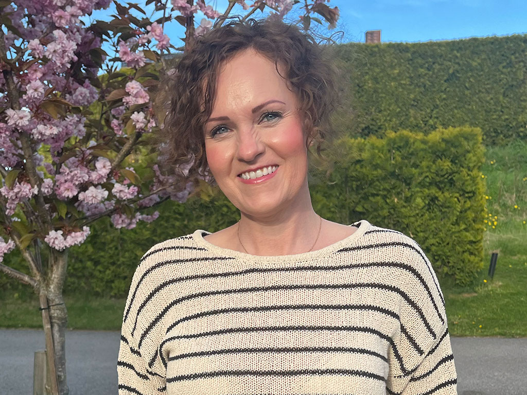 Kvinne står utendørs med frodig bakgrunn