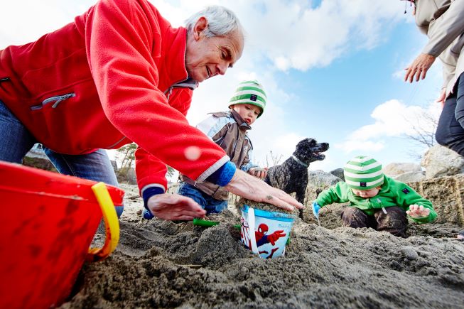 En eldre mann leker med barn i sandkasse