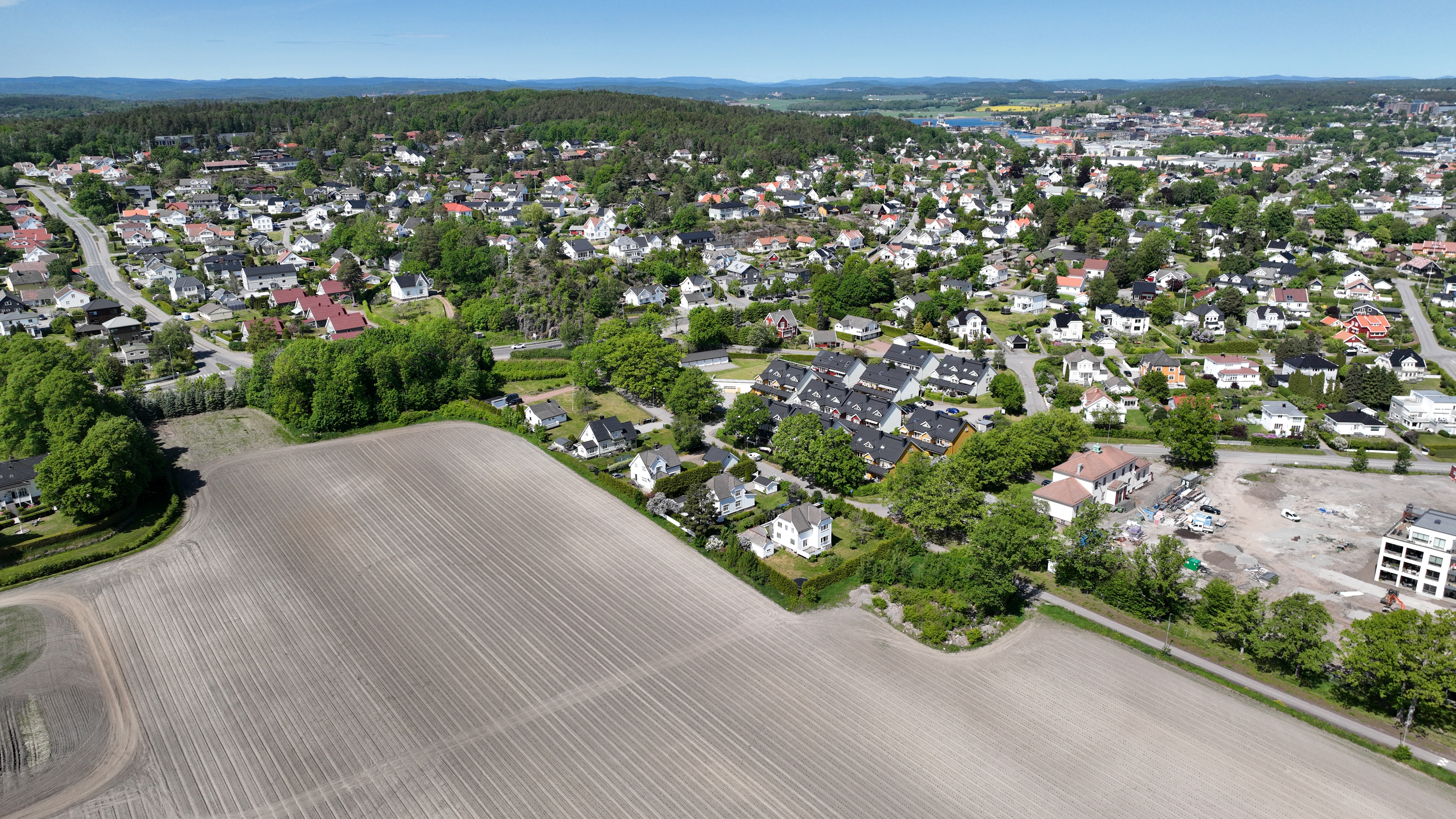 Dronebilde som viser Eikeveien i Færder med jorde i frgrunn og en rekke boligområder emd Teieskogen i bakgrunnen. Deler av Grindløkken i høyre bildekant.
