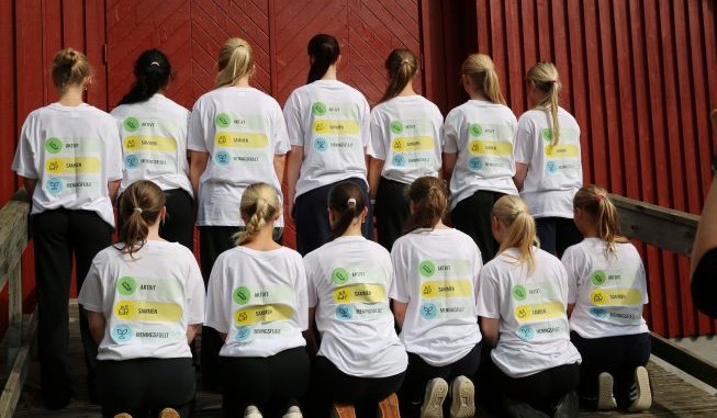 Gruppe av jenter som sitter med ryggen til i ført t-skjorter med ABC budskap