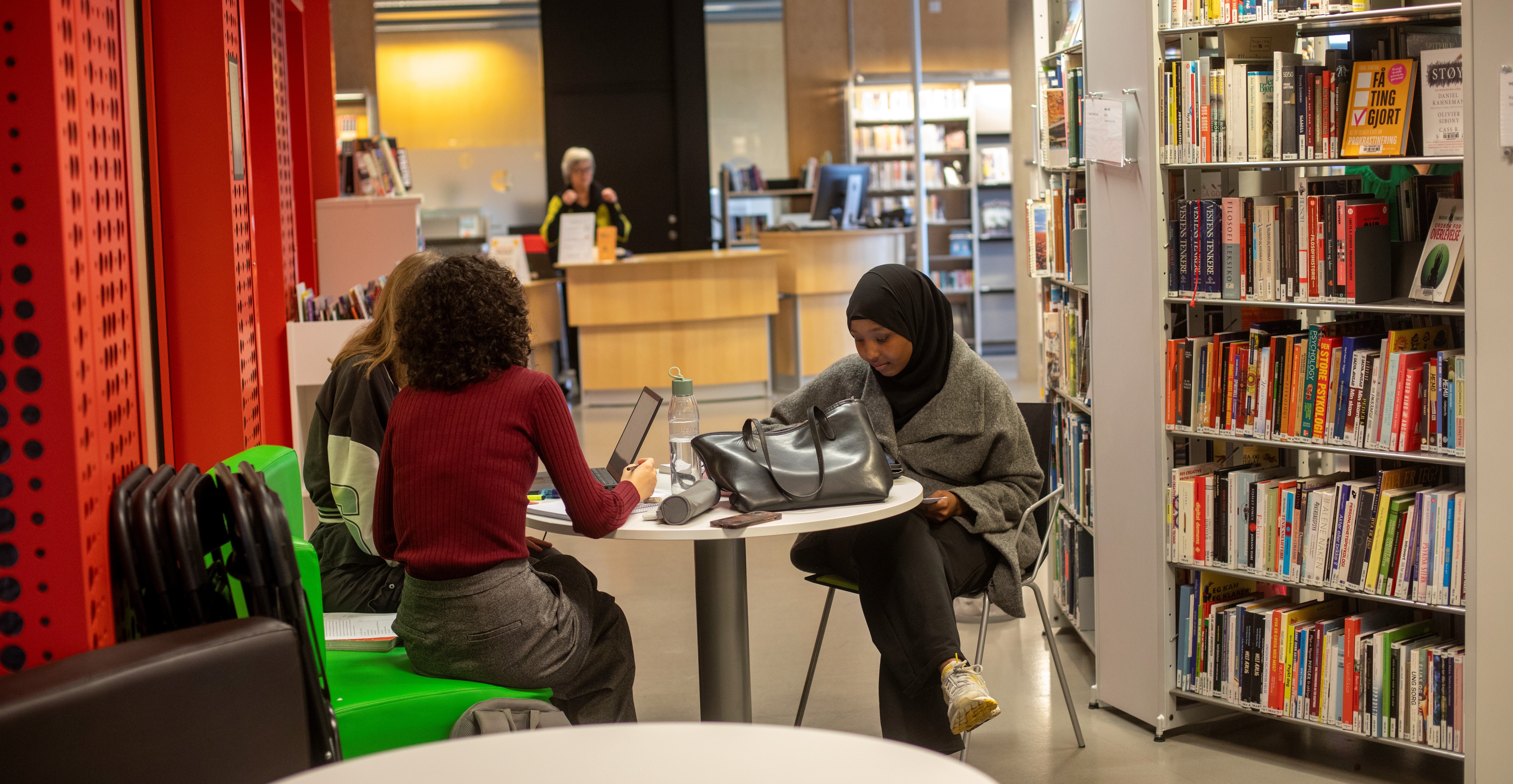 Tre jenter sitter rundt et bord i biblioteket.