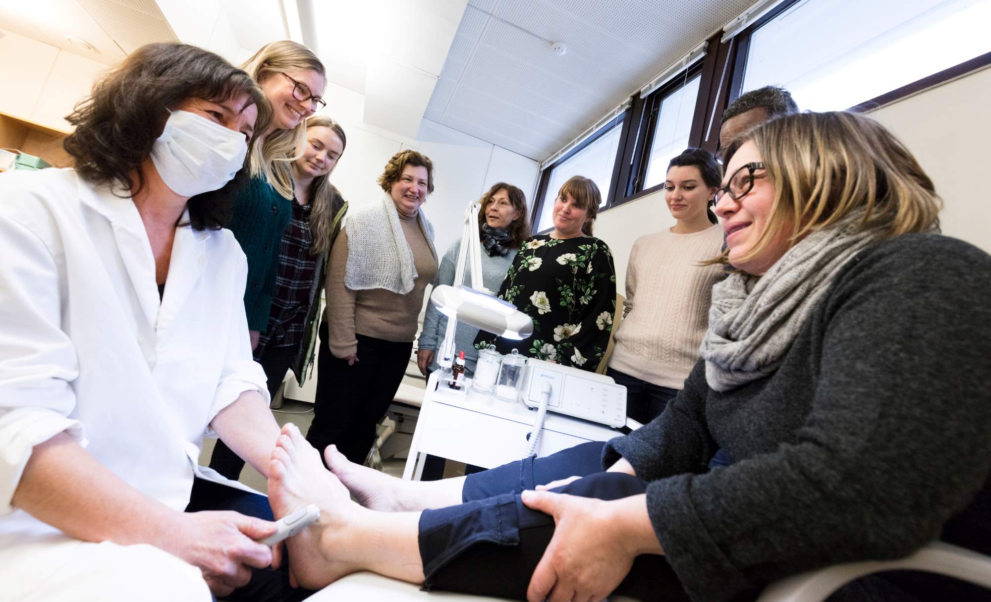 Elever står rundt en lærer som demonstrerer fotpleie på en eldre kunde.