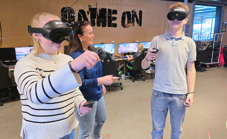 To elever som står med VR-briller og en lærer som instruerer dem.