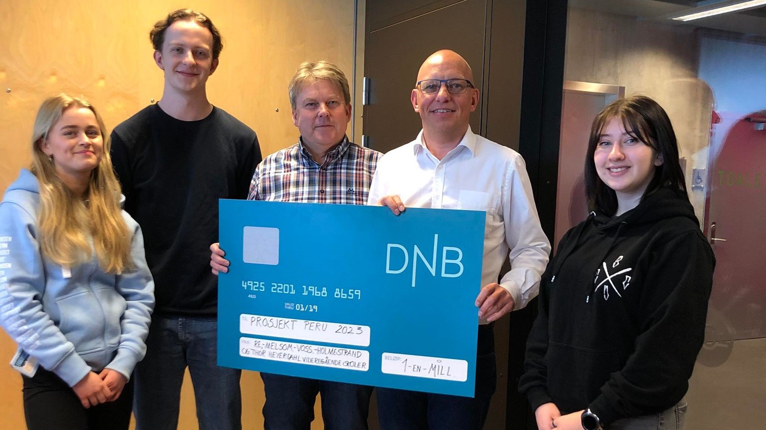 Elever og to menn står sammen og holder en stor sjekk